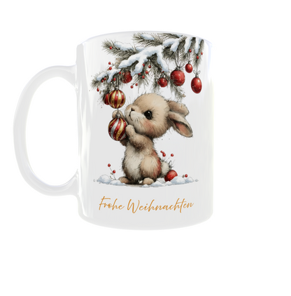 weiße Tasse mit Häschen, das hängt rote Kugeln an einen beschneiten Tannenzweig, unten drunter steht Frohe Weihnachten